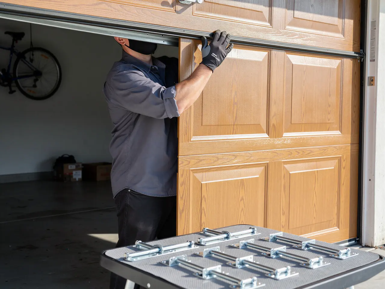 A technician in a mask is installing a light brown garage door.